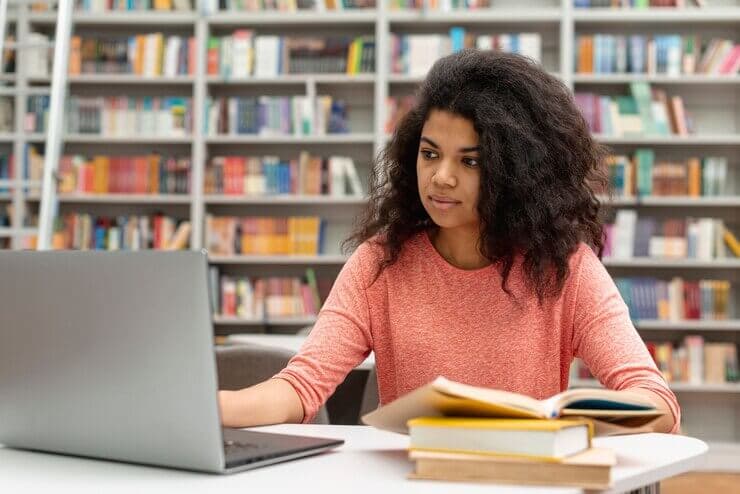 Student studying with laptop and books in a library